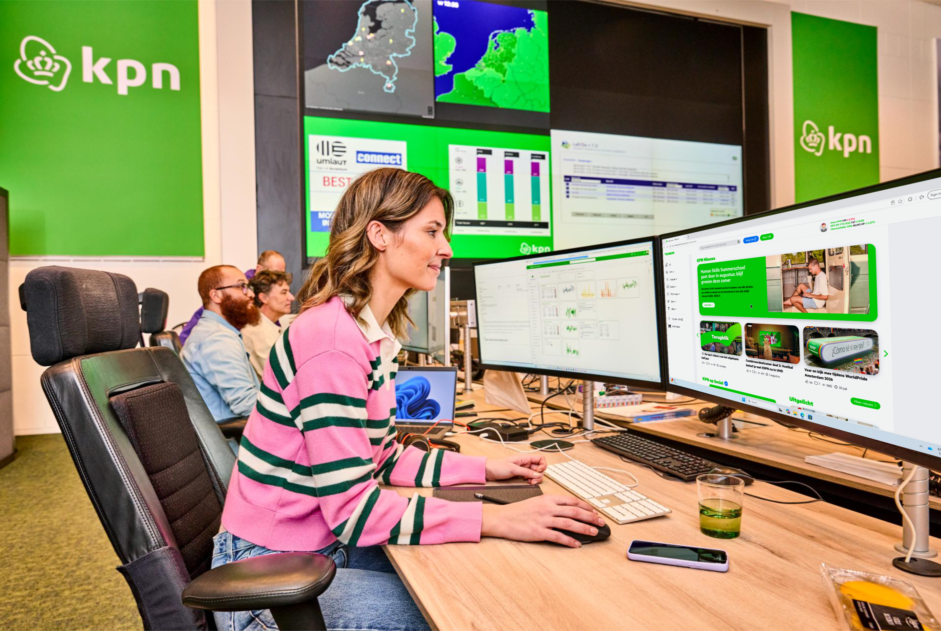 Een KPN-medewerker bekijkt het TEAMKPN-platform op haar beeldscherm, met nieuws en uitgelichte artikelen, in een kantoor met groene KPN-branding.